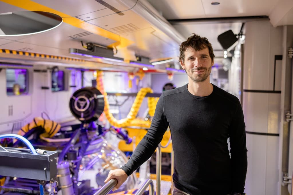 Eric Stackpole on a research vessel beside submersible equipment, with an acrylic dome and instrument racks in the background.