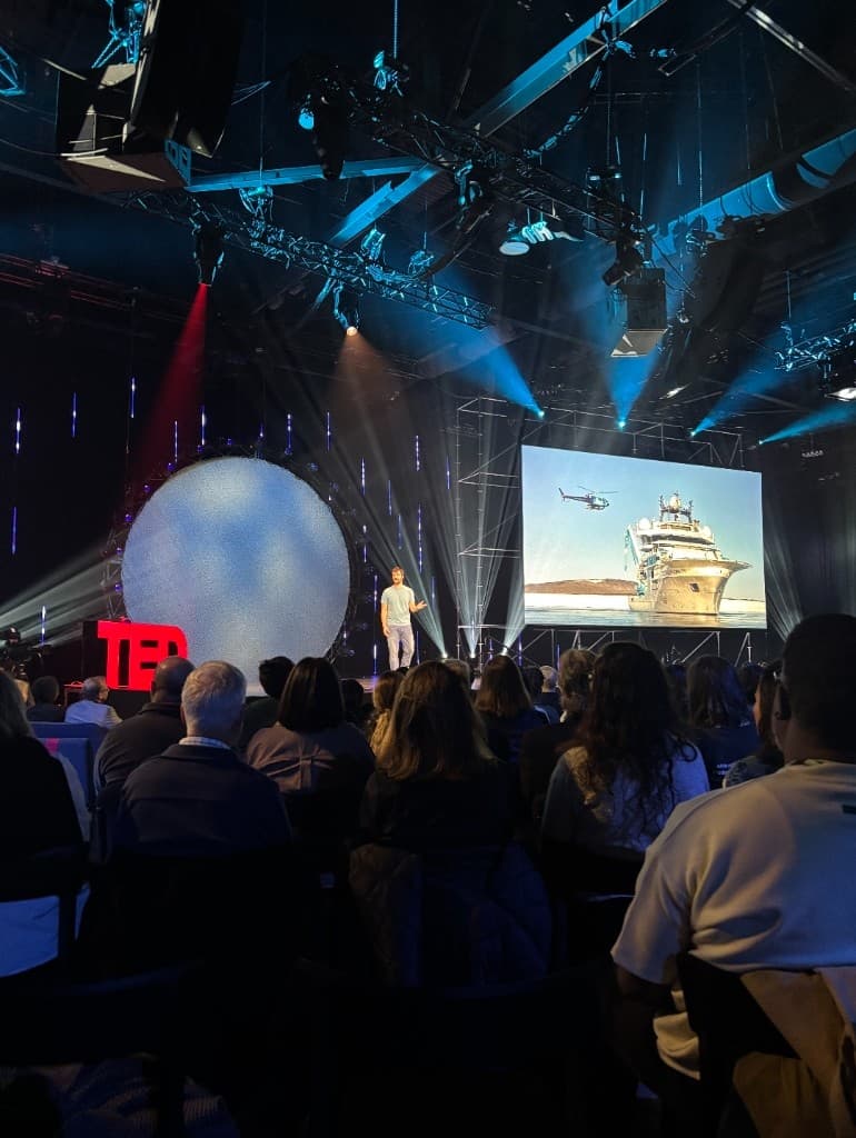 Eric Stackpole on the TED stage, with the audience and stage screens visible.